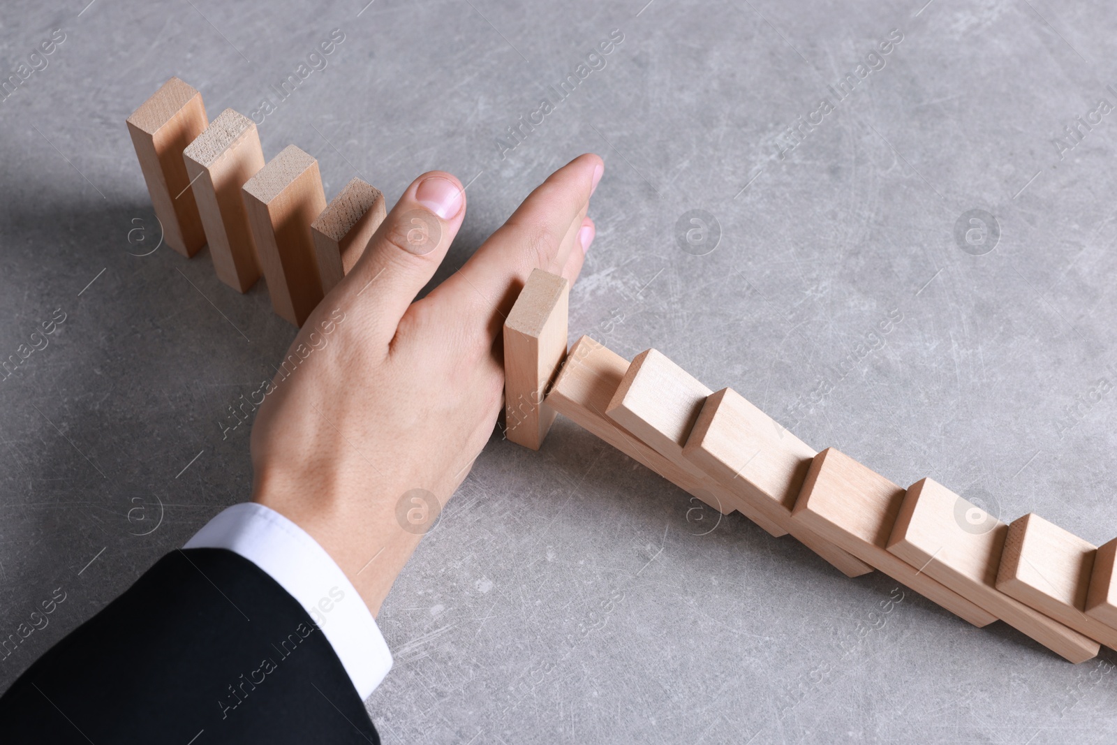 Photo of Man stopping wooden blocks from falling at table, closeup. Domino effect