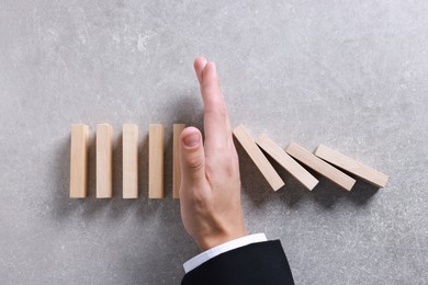 Photo of Man stopping wooden blocks from falling on grey background, top view. Domino effect