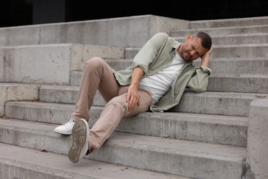 Photo of Man with injured leg and head on stairs outdoors after fall. Dangerous accident