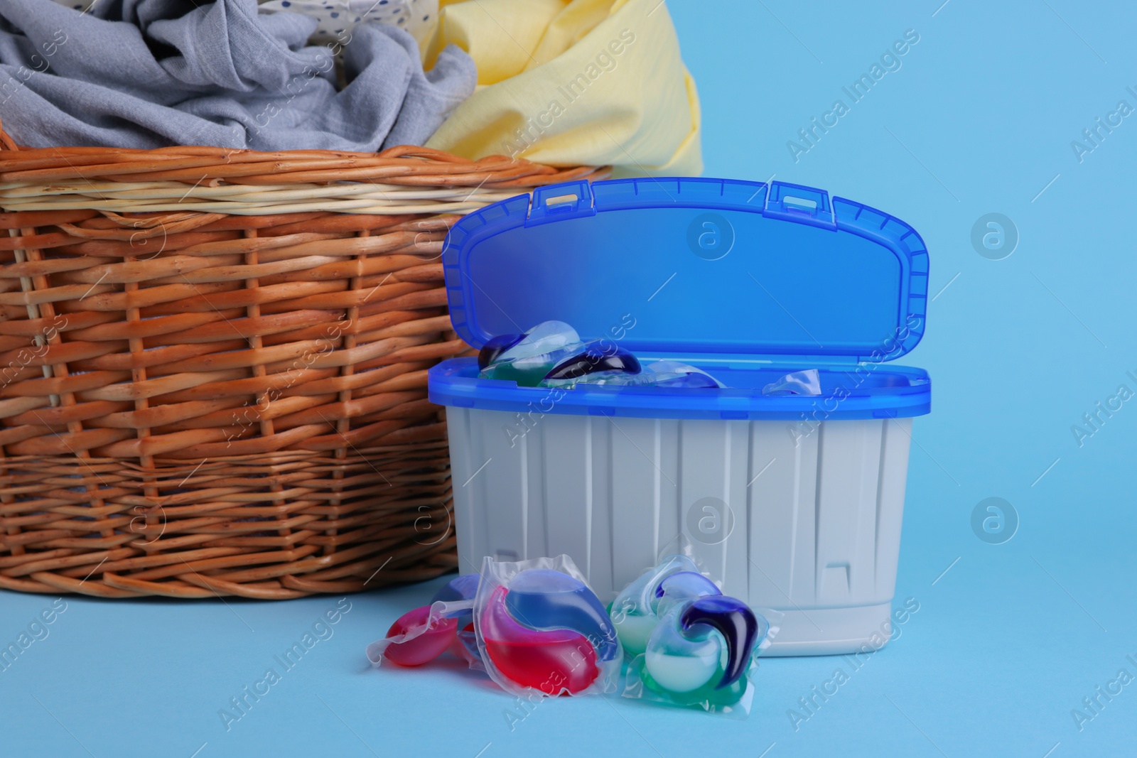 Photo of Detergent capsules and laundry basket on light blue background