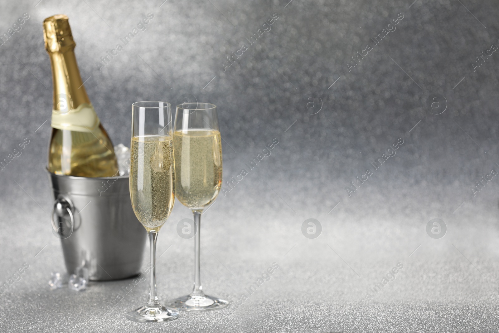 Photo of Champagne in glasses and ice bucket with bottle on silver background. Space for text