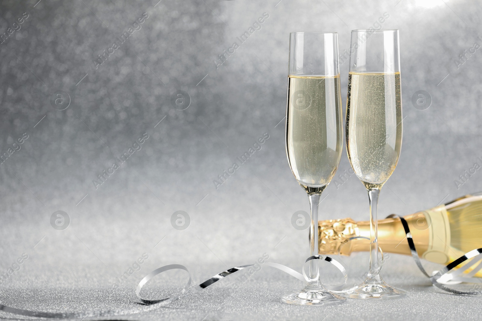 Photo of Champagne in glasses and bottle on silver background. Space for text