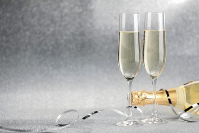 Photo of Champagne in glasses and bottle on silver background. Space for text