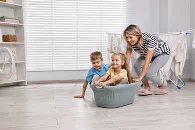 Photo of Happy housewife and her kids playing together in laundry room, space for text