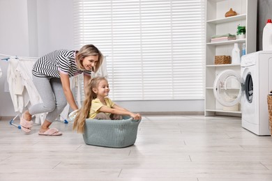 Photo of Happy housewife and her daughter playing together in laundry room, space for text