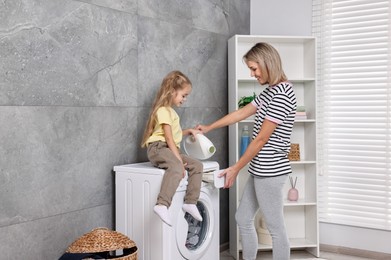 Photo of Housewife and her daughter doing laundry together indoors