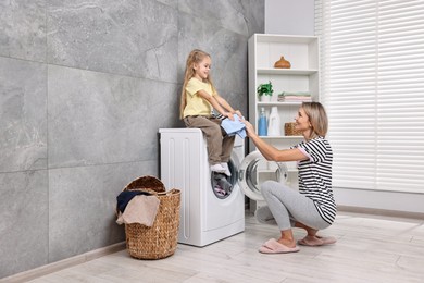 Photo of Housewife and her daughter doing laundry together indoors