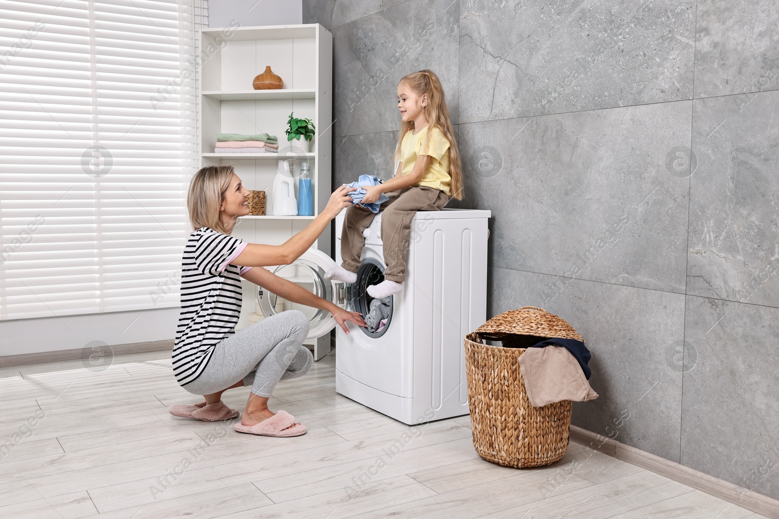 Photo of Housewife and her daughter doing laundry together indoors