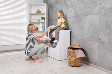 Photo of Housewife and her daughter doing laundry together indoors