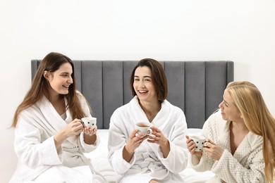 Photo of Spa day. Beautiful women in bathrobes having tea together on bed indoors