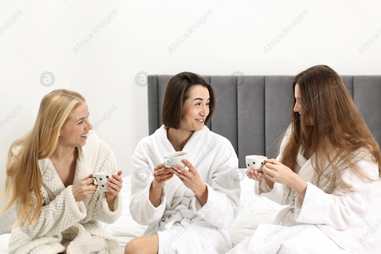 Photo of Spa day. Beautiful women in bathrobes having tea together on bed indoors