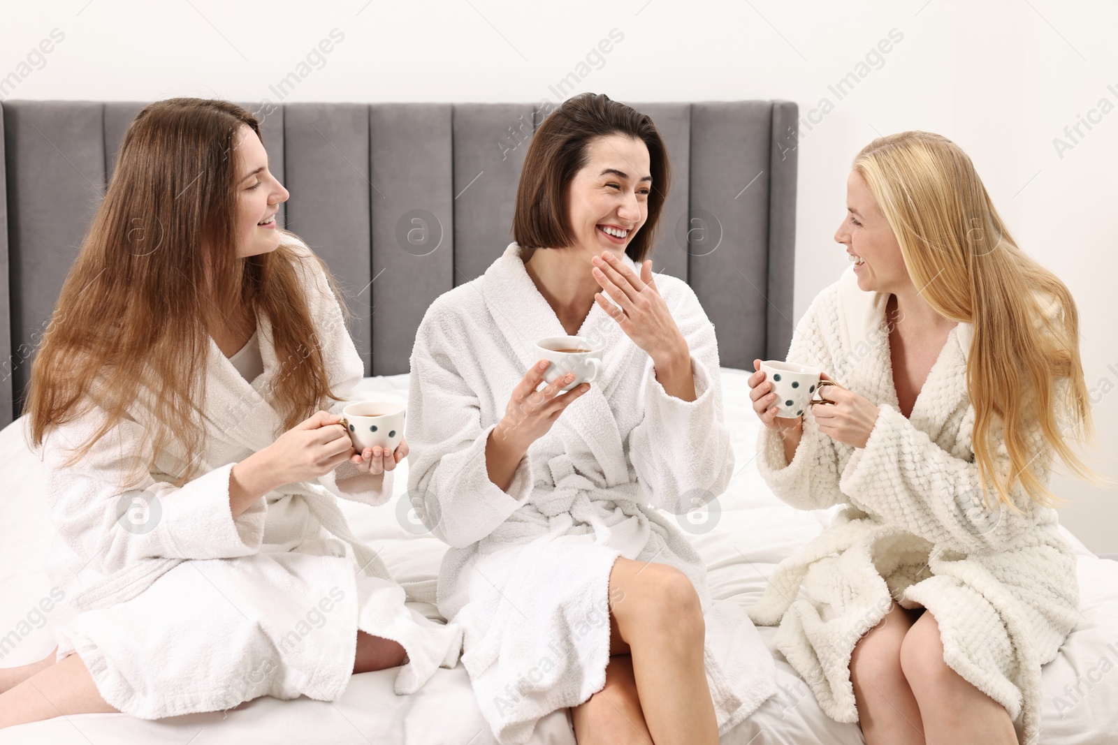 Photo of Spa day. Beautiful women in bathrobes having tea together on bed indoors