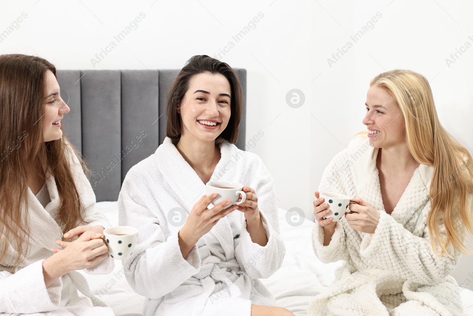 Photo of Spa day. Beautiful women in bathrobes having tea together on bed indoors