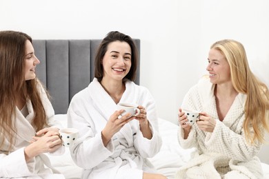 Photo of Spa day. Beautiful women in bathrobes having tea together on bed indoors