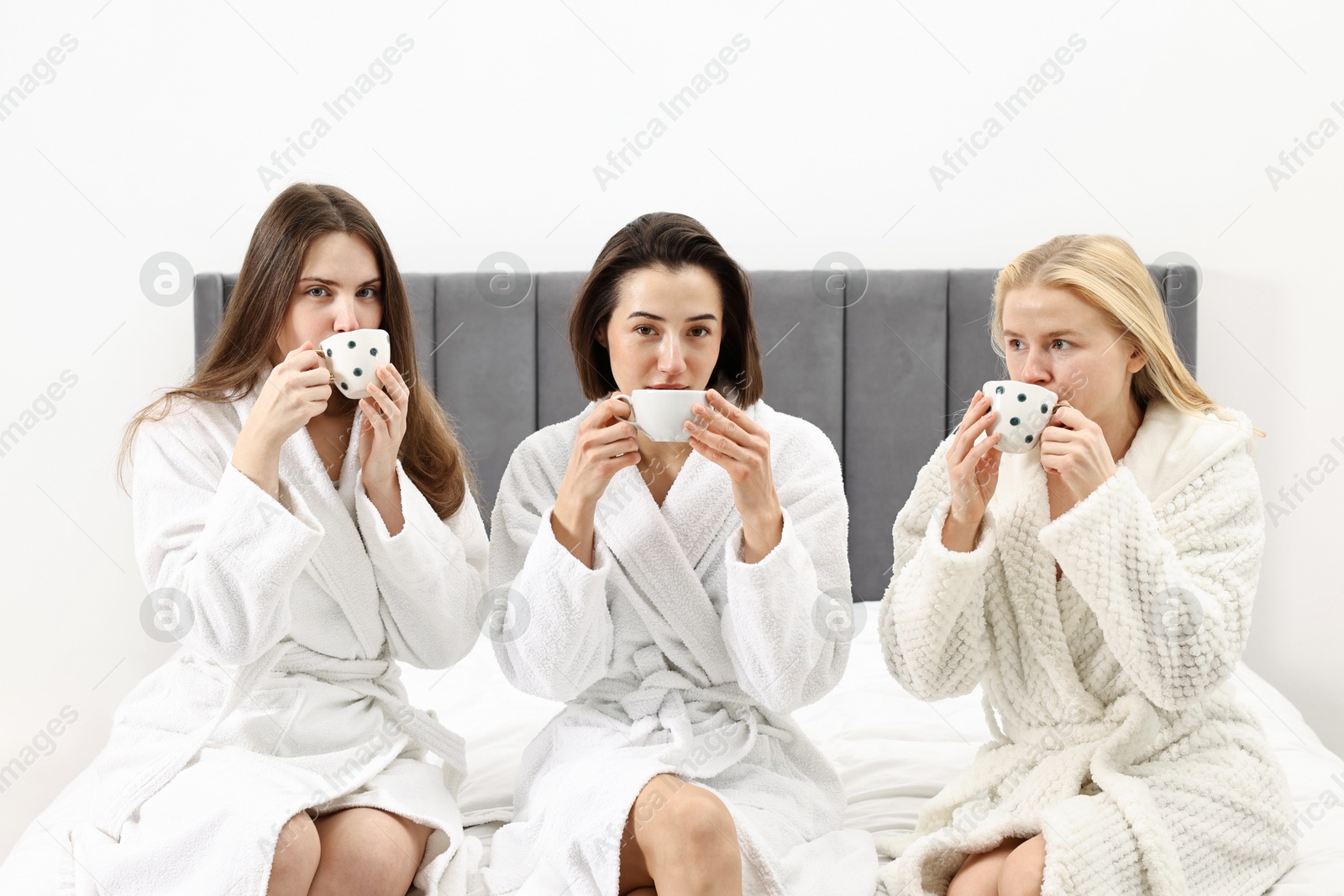 Photo of Spa day. Beautiful women in bathrobes having tea together on bed indoors