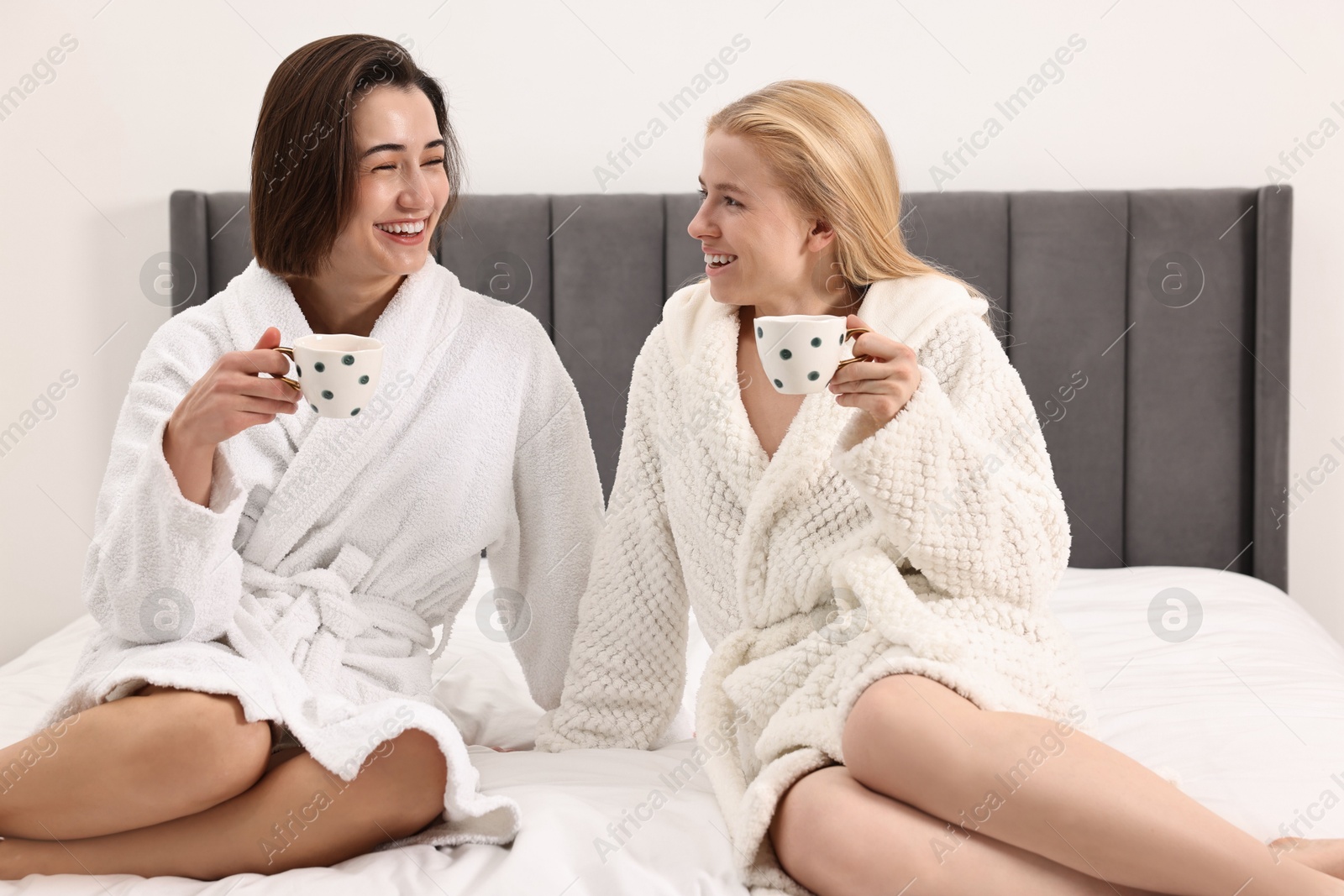 Photo of Spa day. Beautiful women in bathrobes having tea together on bed indoors