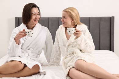 Photo of Spa day. Beautiful women in bathrobes having tea together on bed indoors