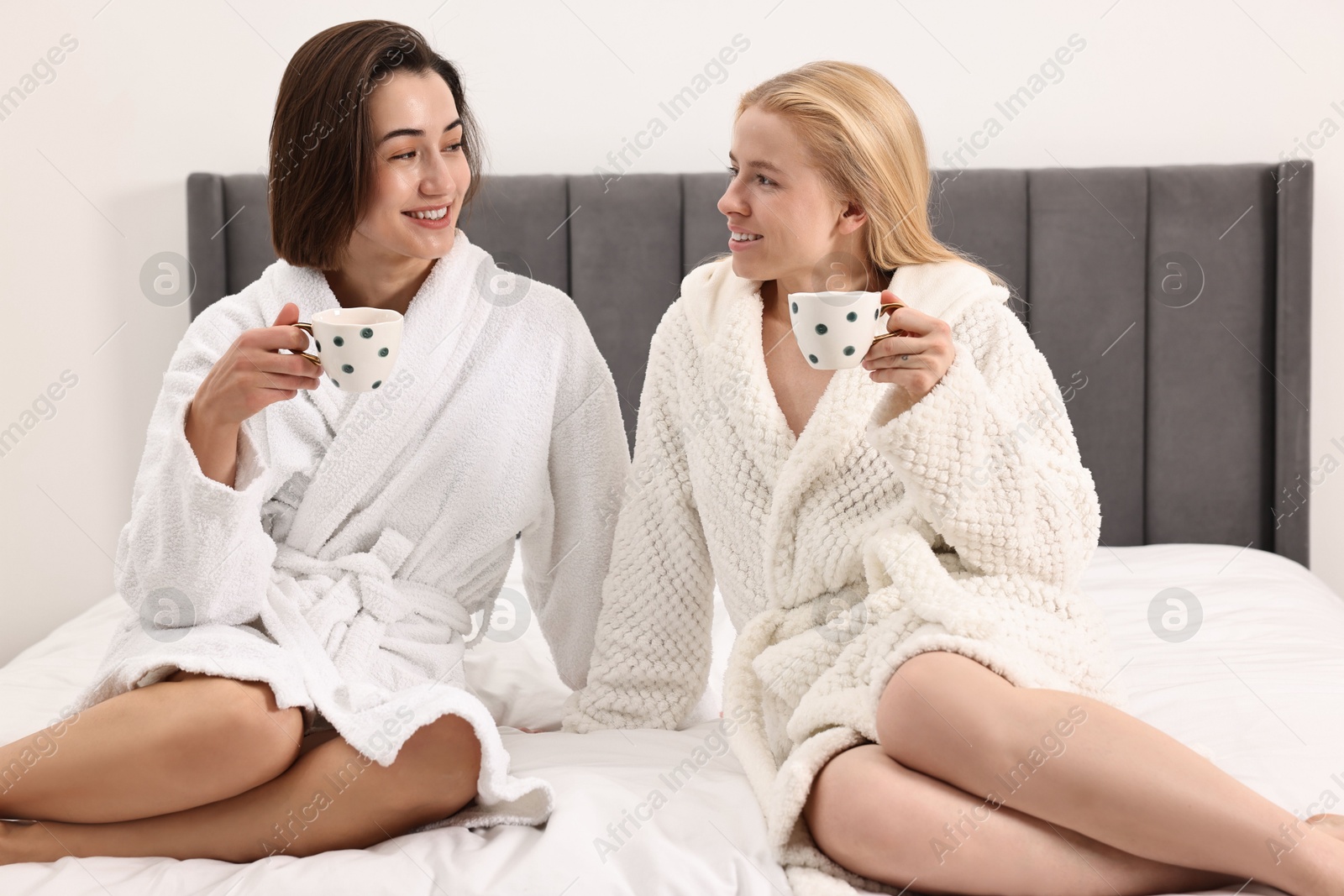 Photo of Spa day. Beautiful women in bathrobes having tea together on bed indoors