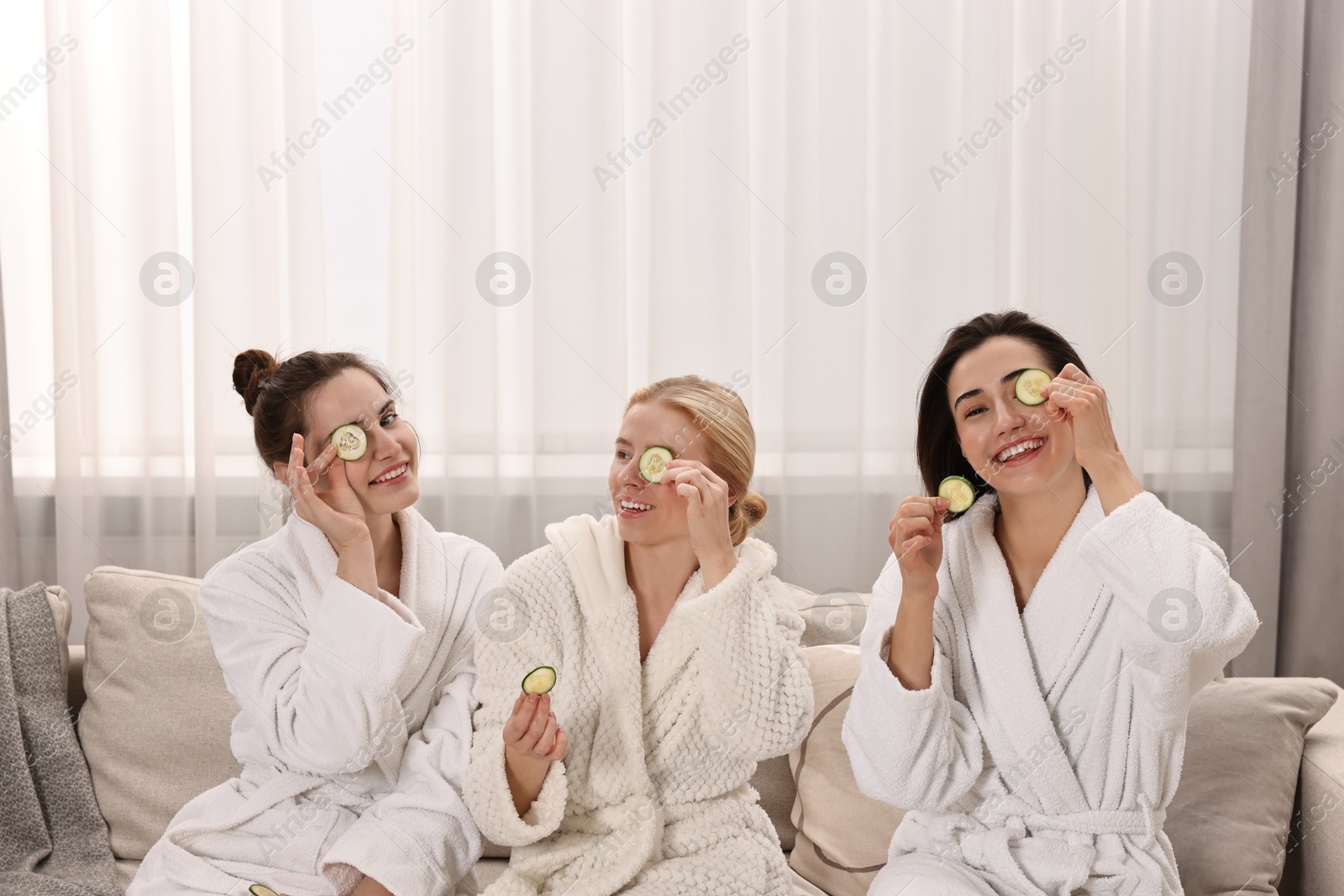 Photo of Happy women with cucumber slices on sofa in spa