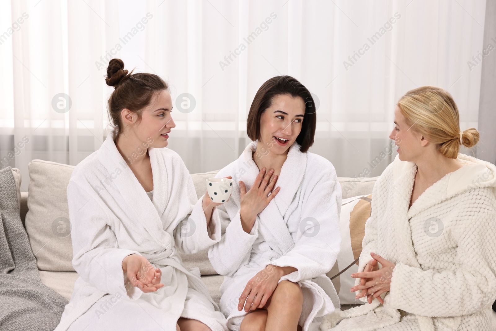 Photo of Cheerful women in bathrobes resting on sofa at spa