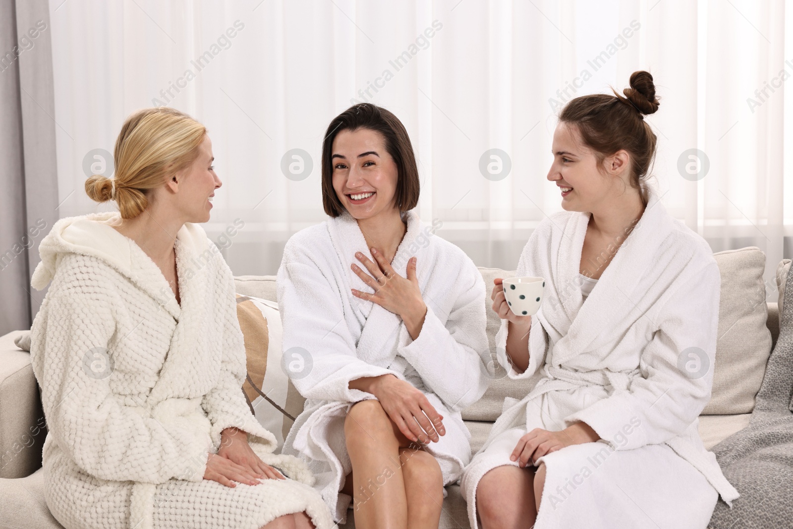 Photo of Cheerful women in bathrobes resting on sofa at spa