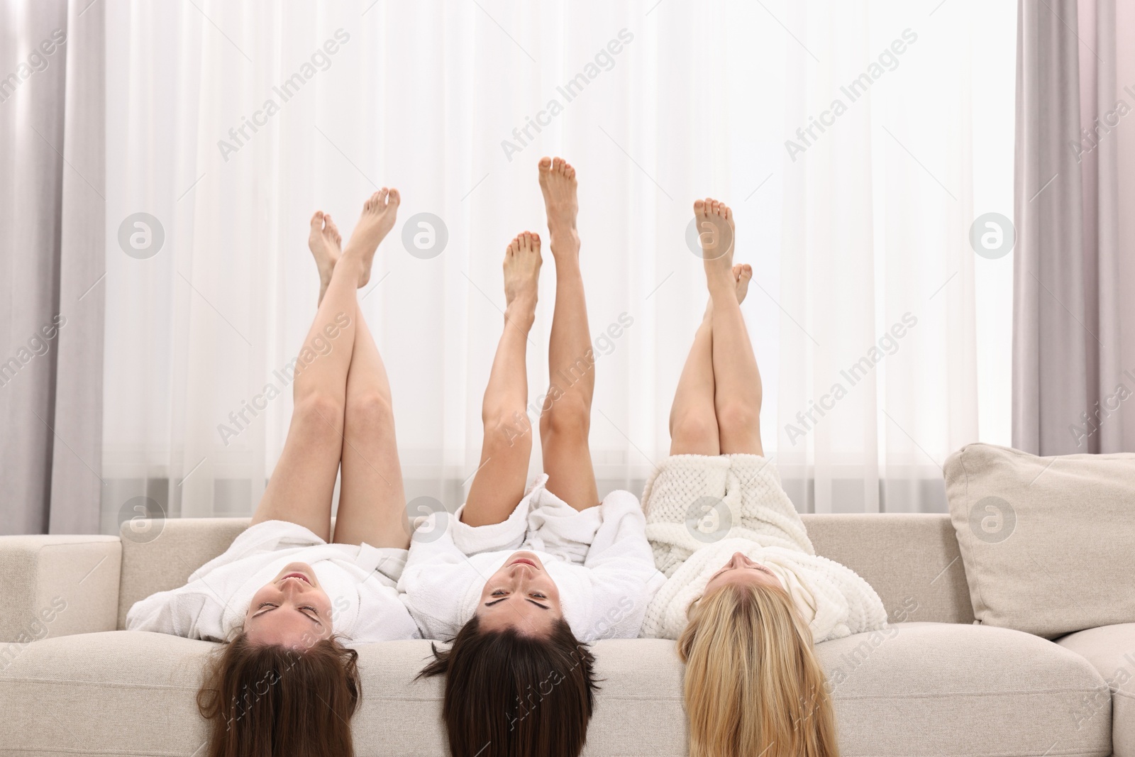 Photo of Spa day. Beautiful women lying with their legs up on sofa indoors