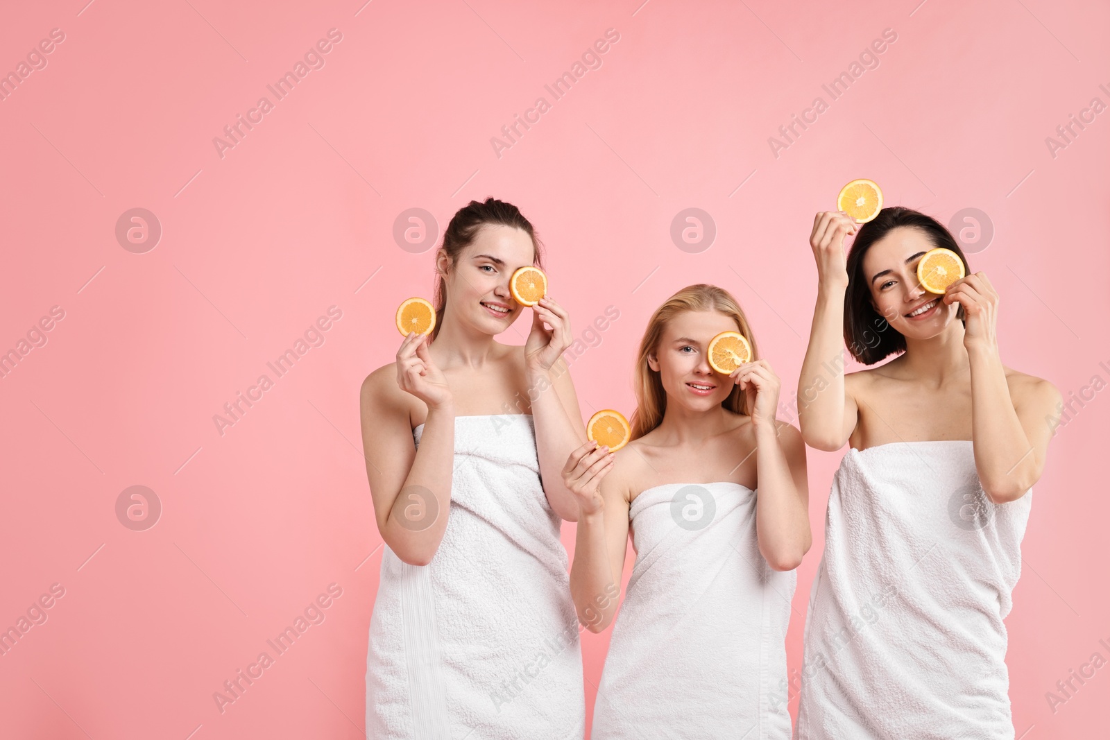 Photo of Spa day. Cheerful women wrapped in towels with orange slices on pink background