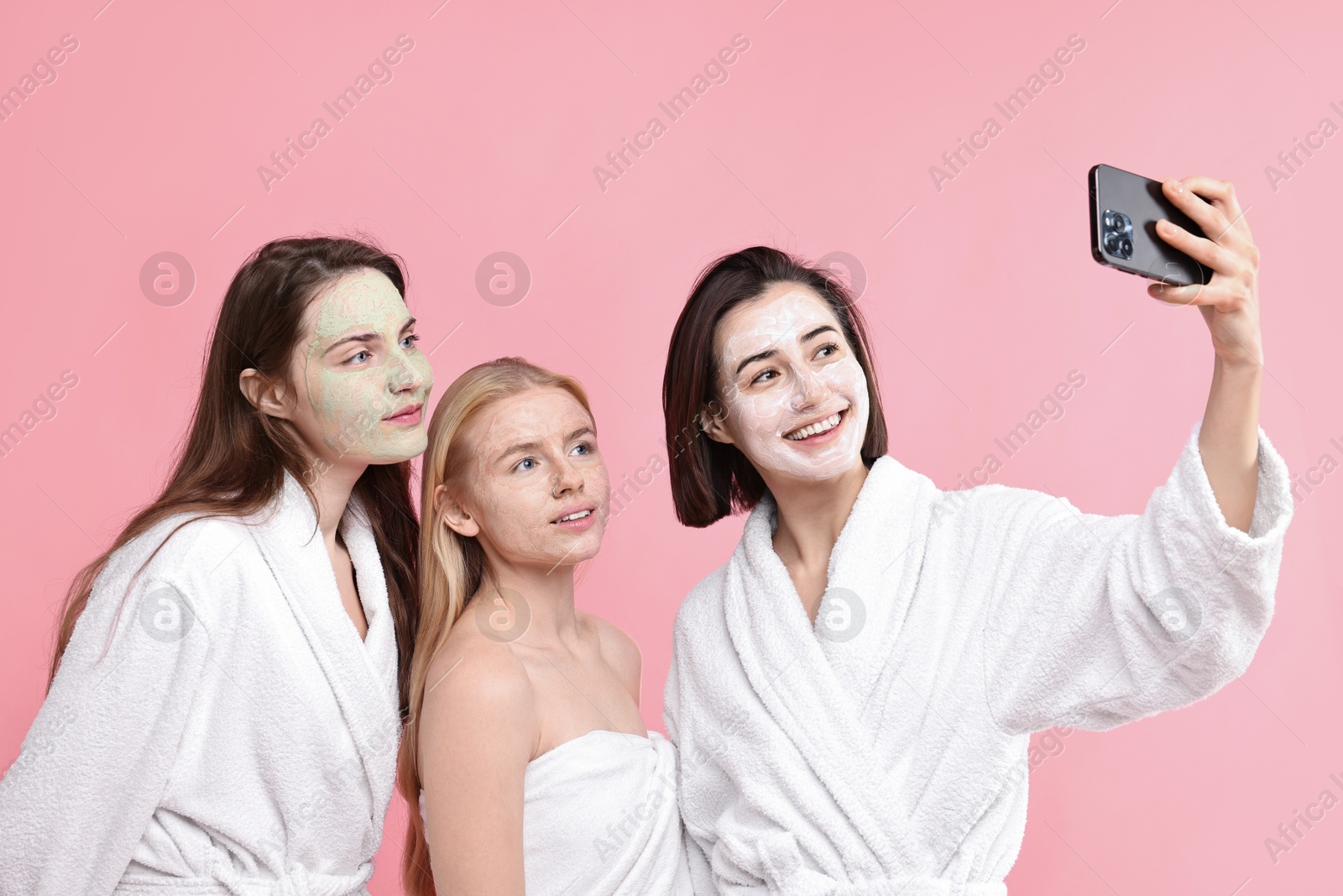 Photo of Spa day. Happy women with face masks taking selfie on pink background