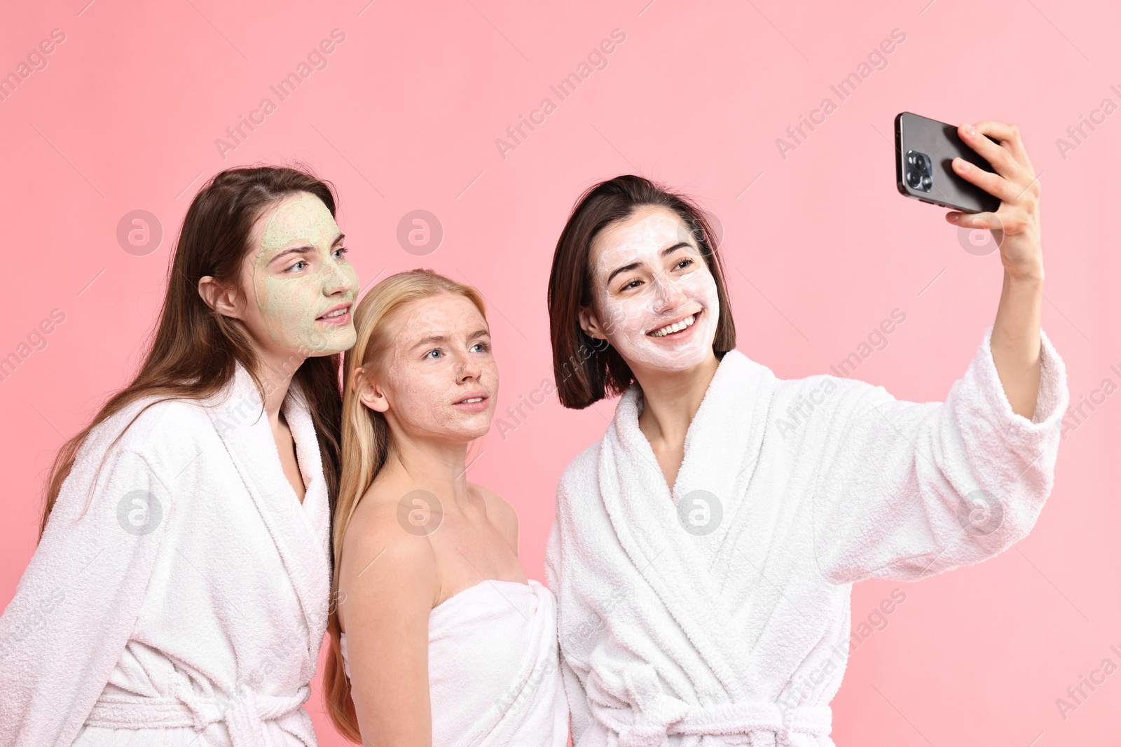 Photo of Spa day. Happy women with face masks taking selfie on pink background