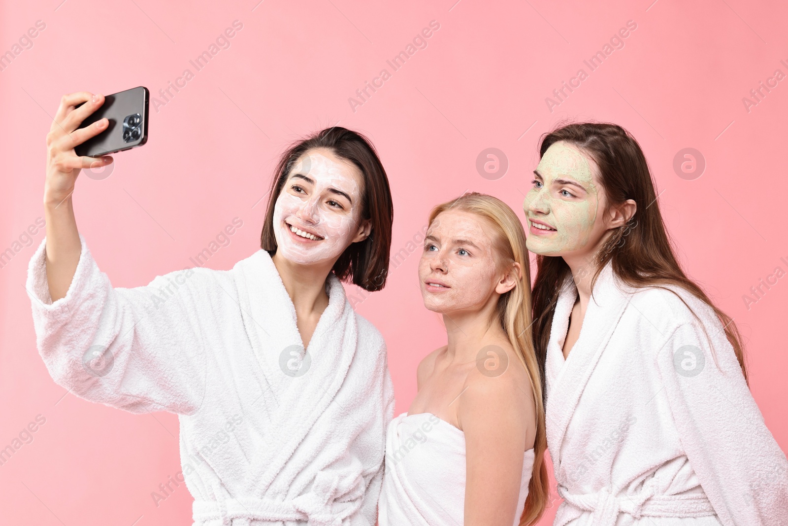 Photo of Spa day. Happy women with face masks taking selfie on pink background