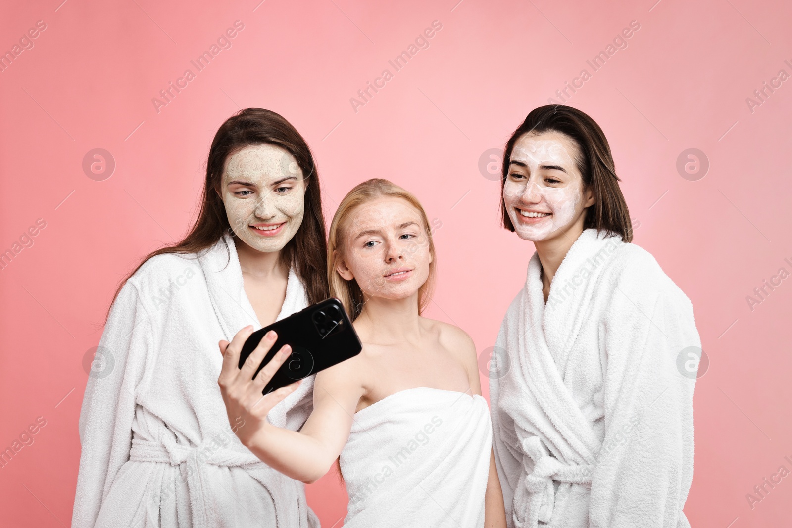 Photo of Spa day. Happy women with face masks taking selfie on pink background