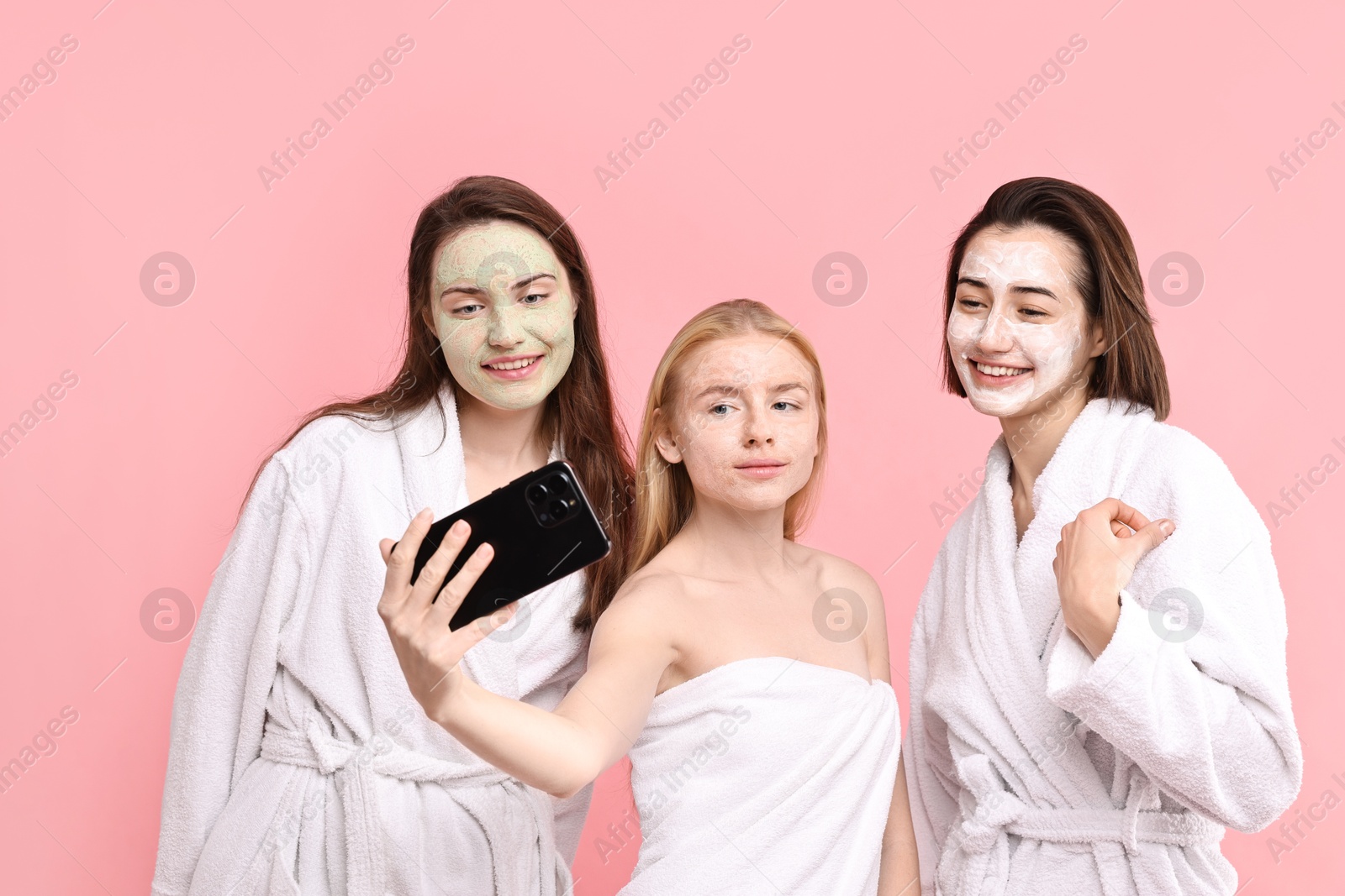 Photo of Spa day. Happy women with face masks taking selfie on pink background