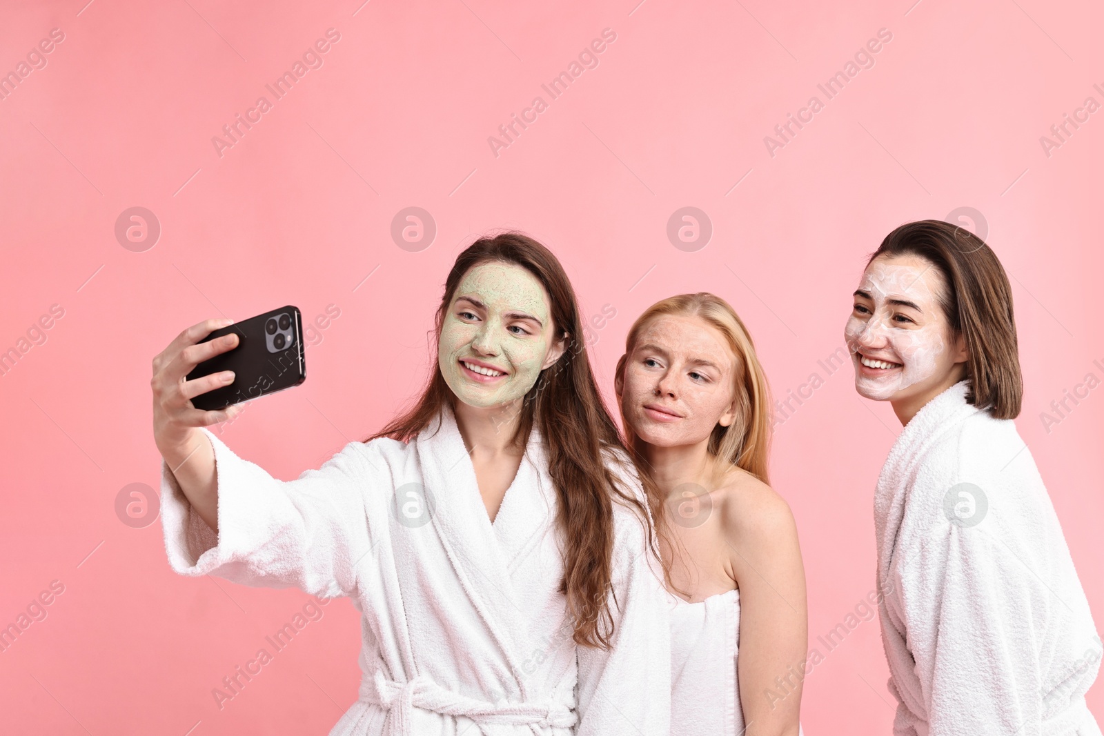 Photo of Spa day. Happy women with face masks taking selfie on pink background