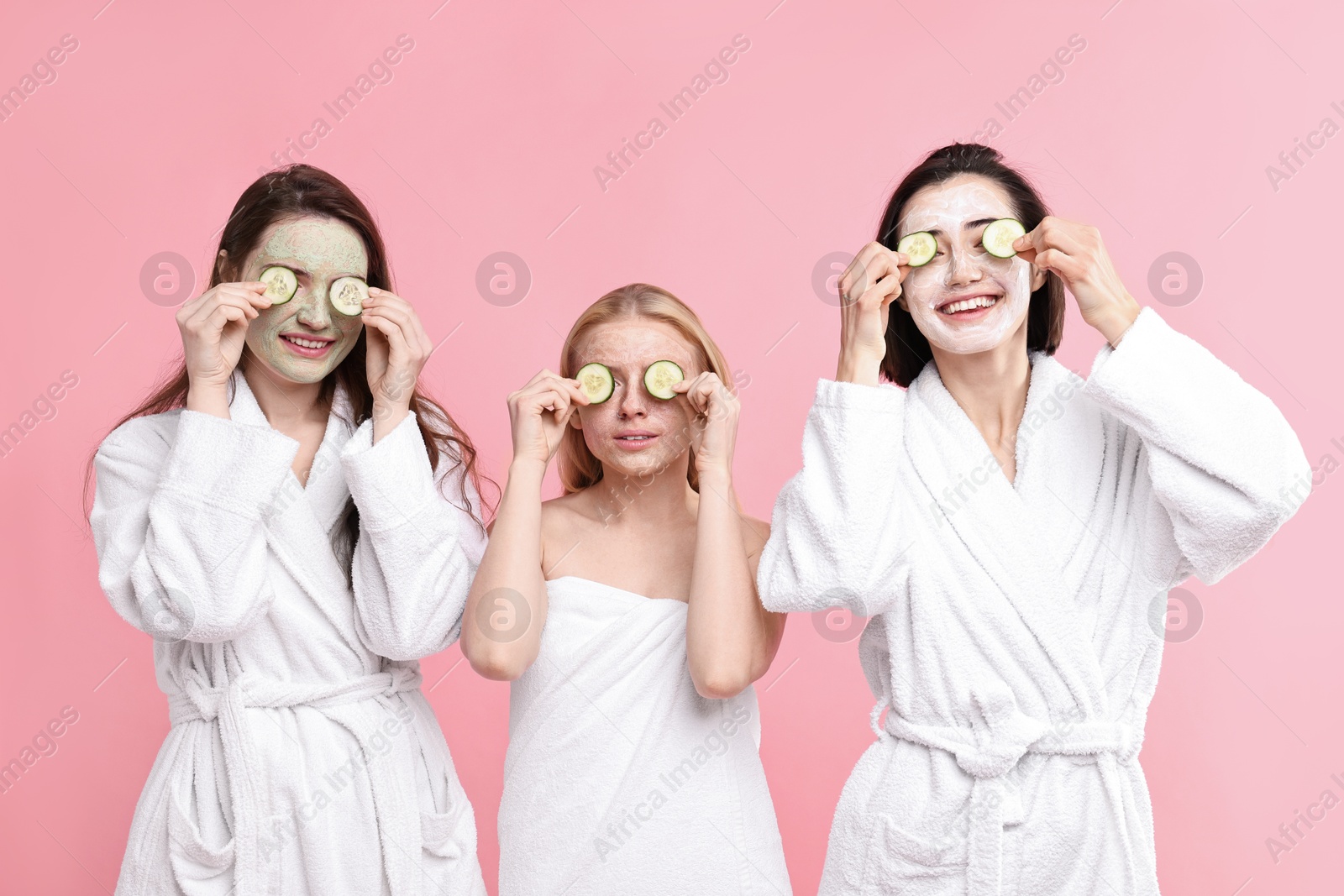 Photo of Spa day. Happy women with face masks and cucumber slices on pink background