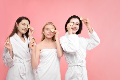 Photo of Spa day. Happy women with face masks and cucumber slices on pink background