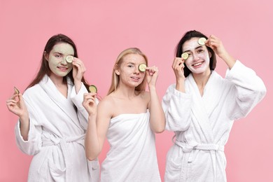 Photo of Spa day. Happy women with face masks and cucumber slices on pink background