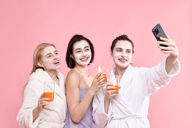 Photo of Spa day. Beautiful women with face masks and healthy drinks taking selfie on pink background