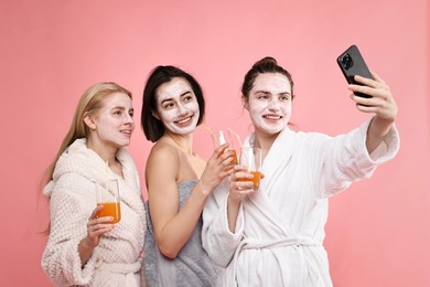 Photo of Spa day. Beautiful women with face masks and healthy drinks taking selfie on pink background