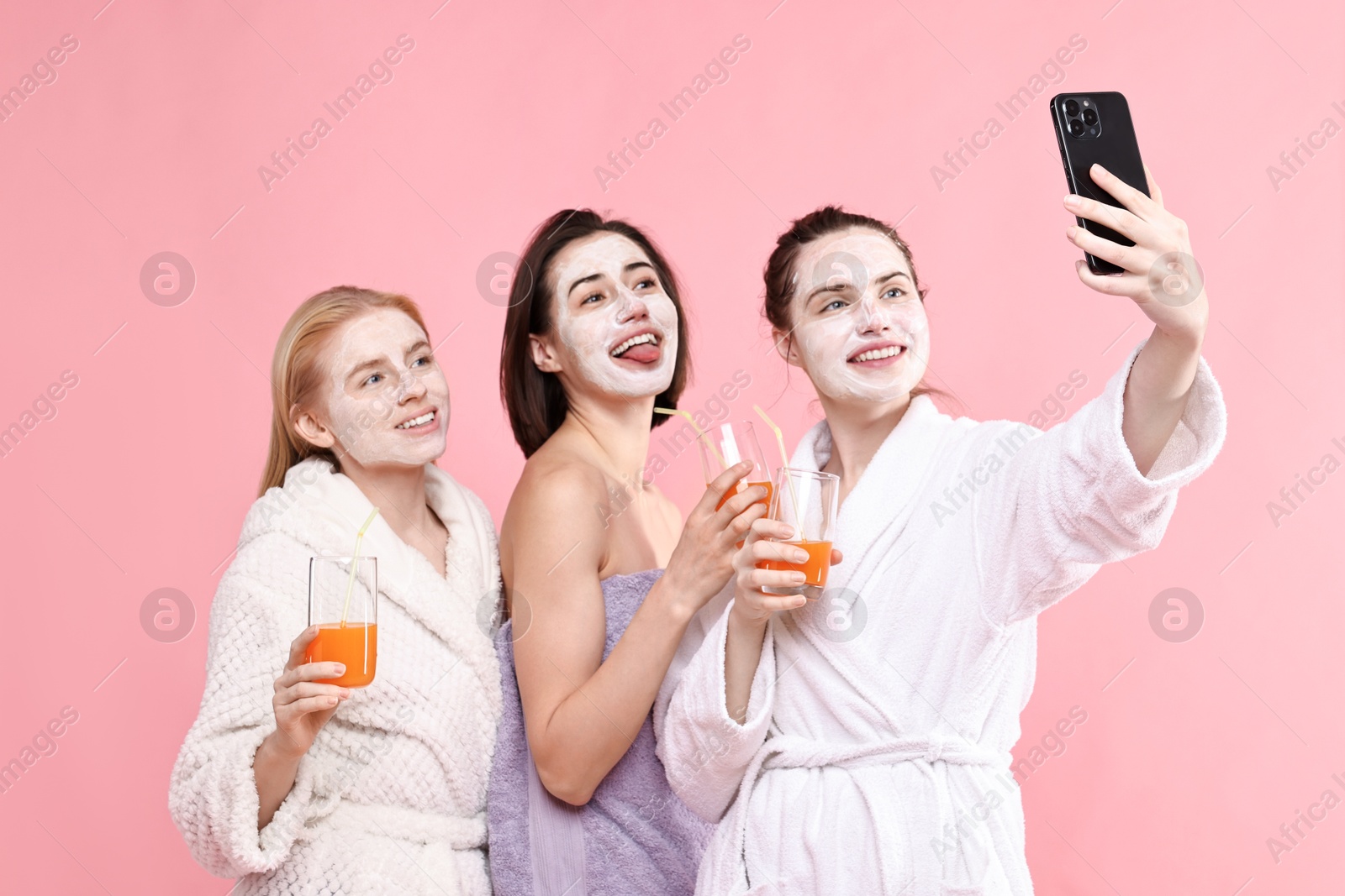 Photo of Spa day. Beautiful women with face masks and healthy drinks taking selfie on pink background