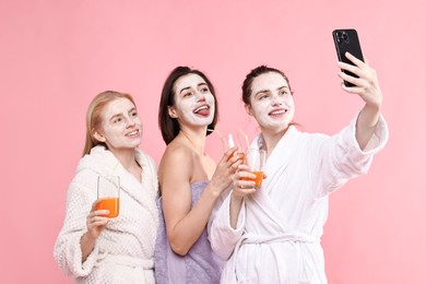 Photo of Spa day. Beautiful women with face masks and healthy drinks taking selfie on pink background