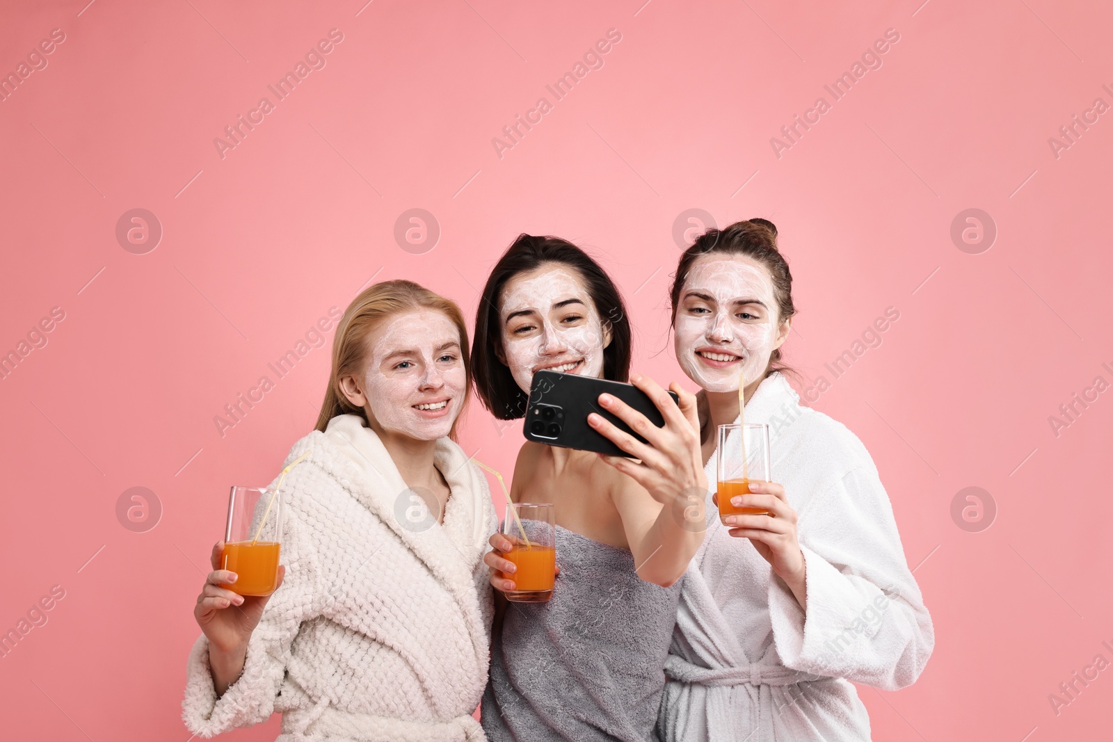 Photo of Spa day. Beautiful women with face masks and healthy drinks taking selfie on pink background