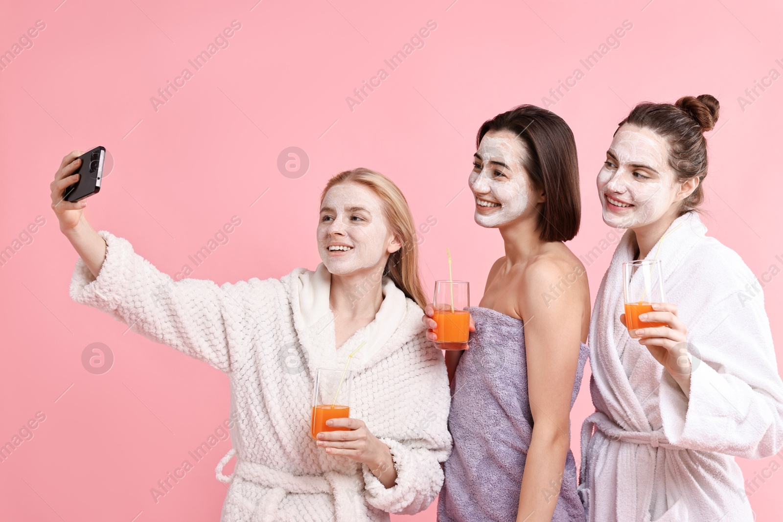 Photo of Spa day. Beautiful women with face masks and healthy drinks taking selfie on pink background