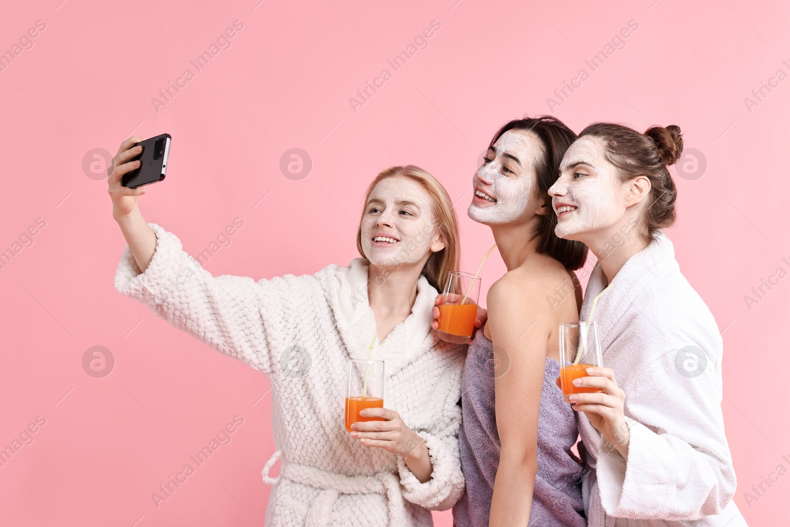 Photo of Spa day. Beautiful women with face masks and healthy drinks taking selfie on pink background