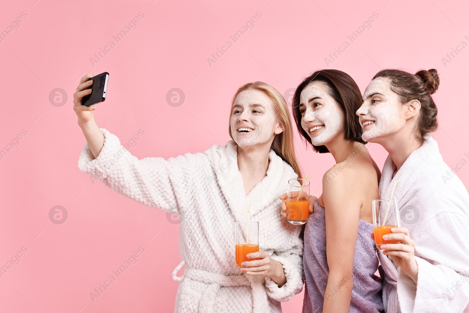 Photo of Spa day. Beautiful women with face masks and healthy drinks taking selfie on pink background