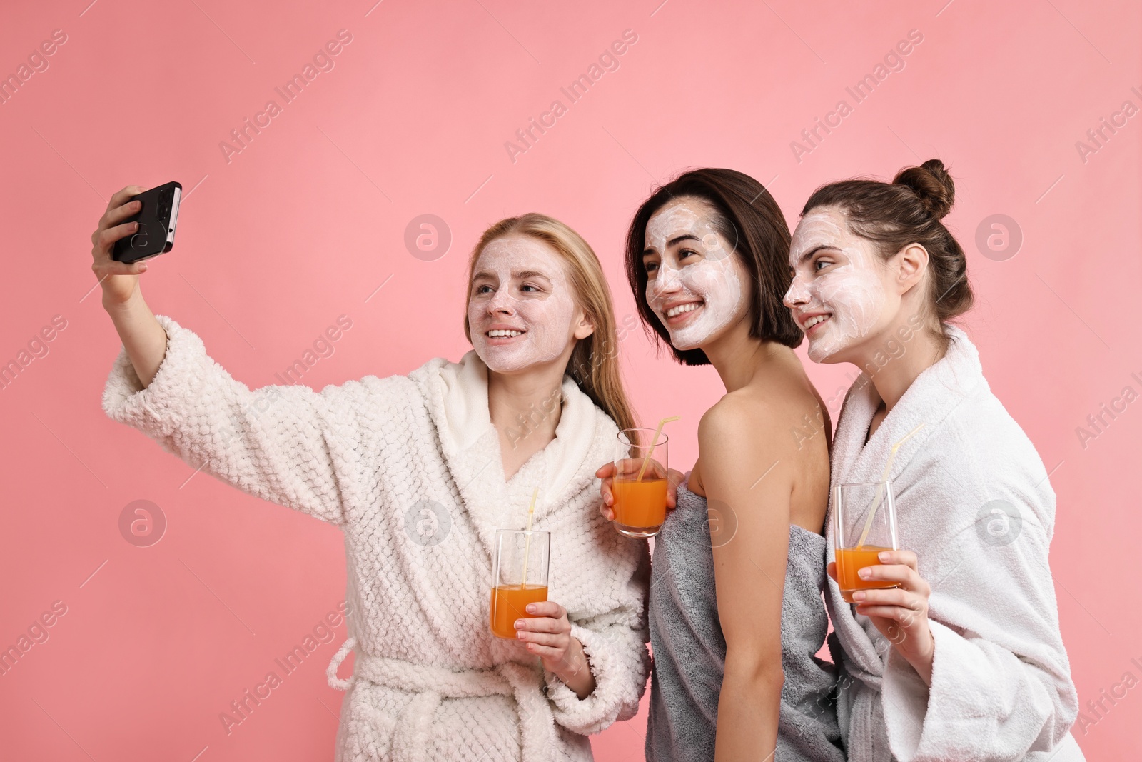 Photo of Spa day. Beautiful women with face masks and healthy drinks taking selfie on pink background