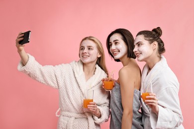 Photo of Spa day. Beautiful women with face masks and healthy drinks taking selfie on pink background