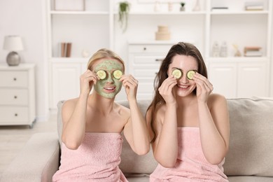 Photo of Spa day. Beautiful women with face masks and cucumber slices on sofa indoors