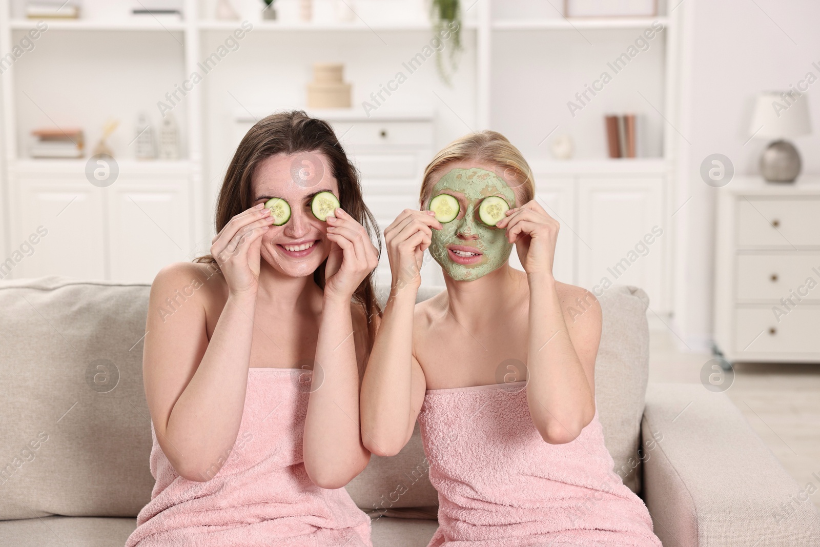 Photo of Spa day. Beautiful women with face masks and cucumber slices on sofa indoors