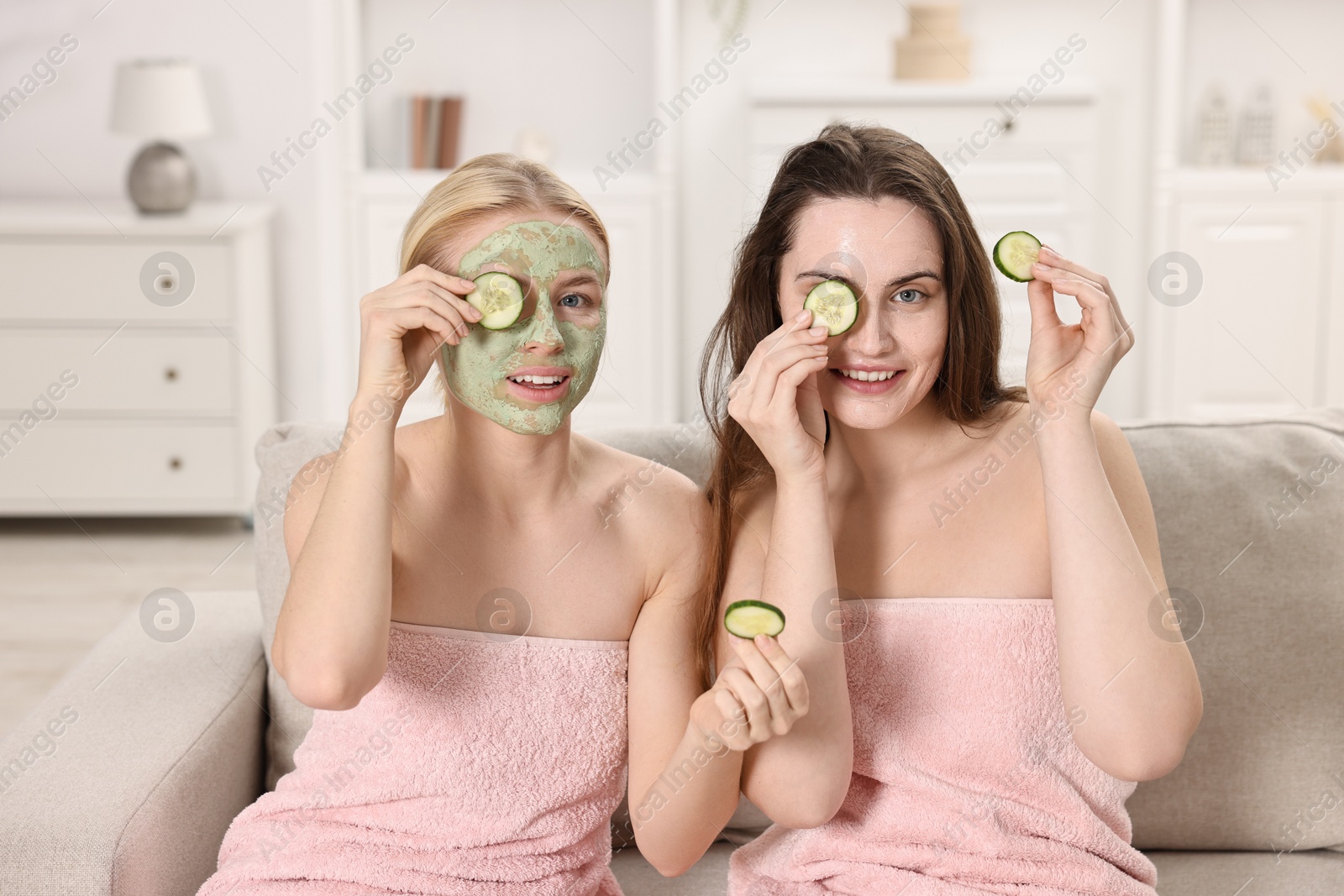 Photo of Spa day. Beautiful women with face masks and cucumber slices on sofa indoors