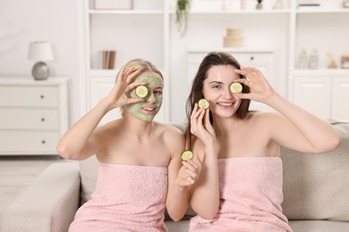 Photo of Spa day. Beautiful women with face masks and cucumber slices on sofa indoors